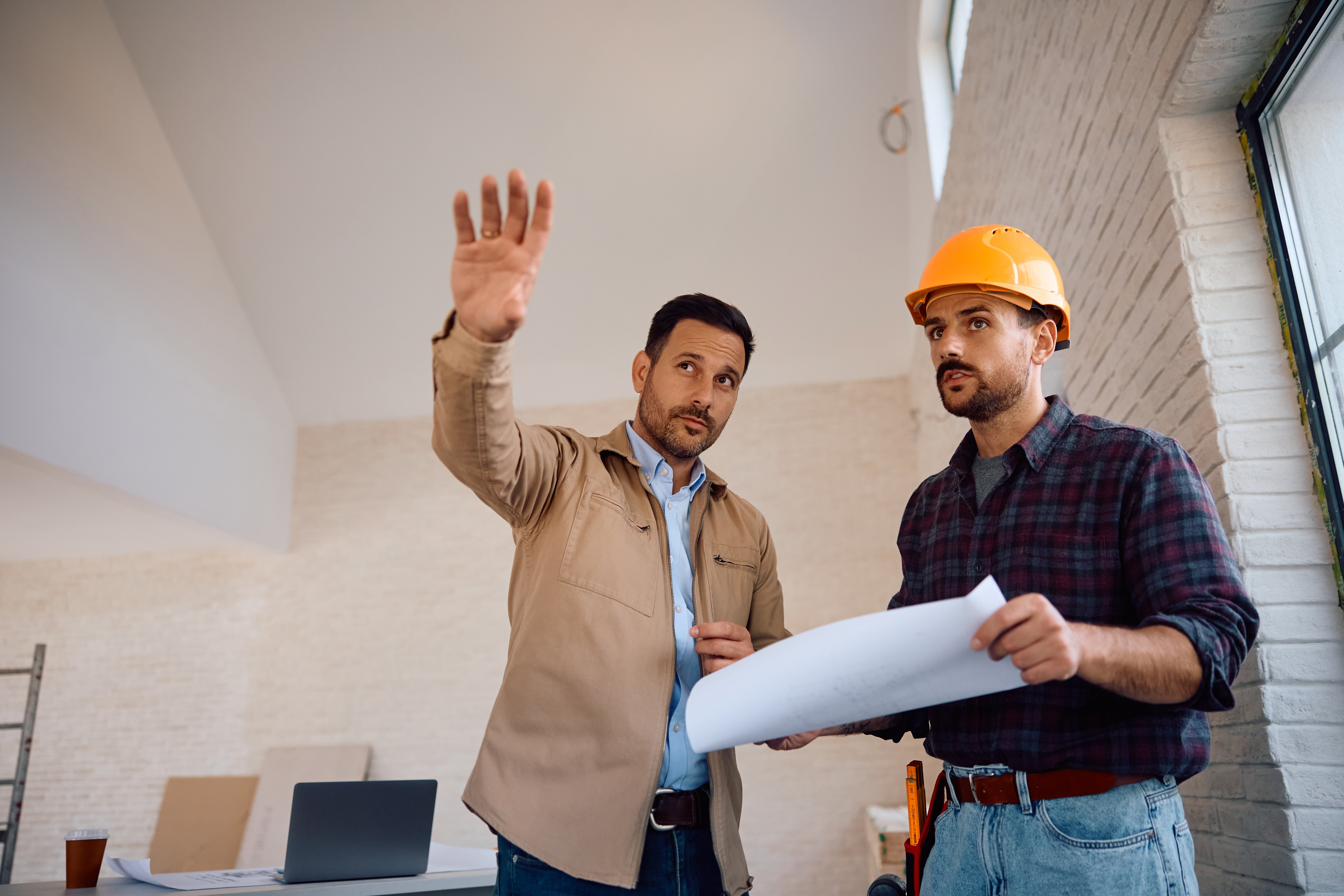 Home owner and manual worker cooperating while analyzing blueprints at construction site. Copy space.